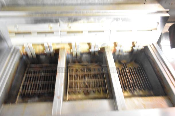Commercial deep fryer with three sections, metal grates, signs of use, ideal for high-volume cooking.