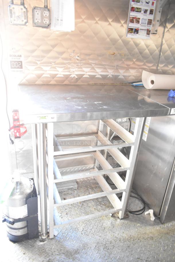 Stainless steel prep table with shelving, Ecolab sanitizer station; diamond-patterned metal wall; fair condition.