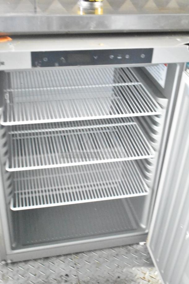 Commercial refrigerator with open door, featuring four wire shelves. Stainless steel exterior, digital control panel on top.