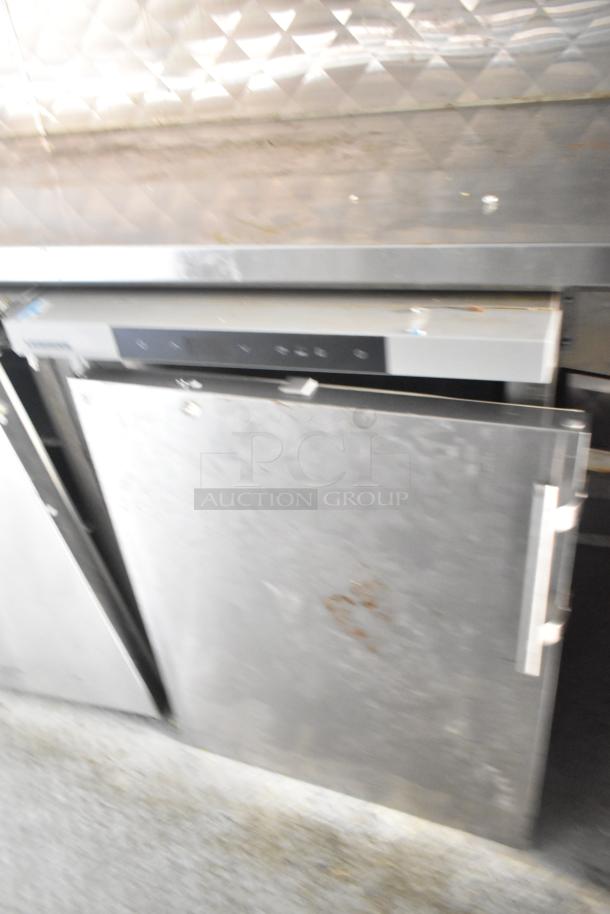 Stainless steel commercial dishwasher with digital control panel, showing signs of wear and rust on the door.