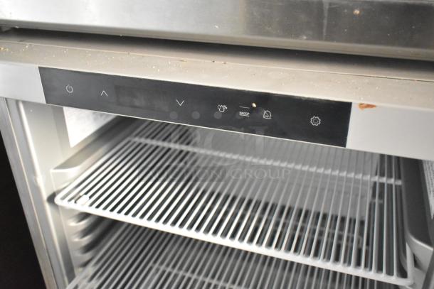 Commercial refrigerator with digital control panel, three wire shelves, and HACCP compliance symbols. Slight surface wear visible.