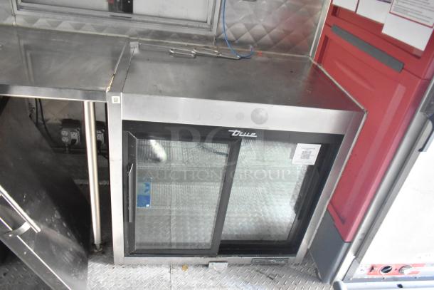True commercial refrigerator with glass front, steel top, and sliding doors. Good condition, QR code label attached.