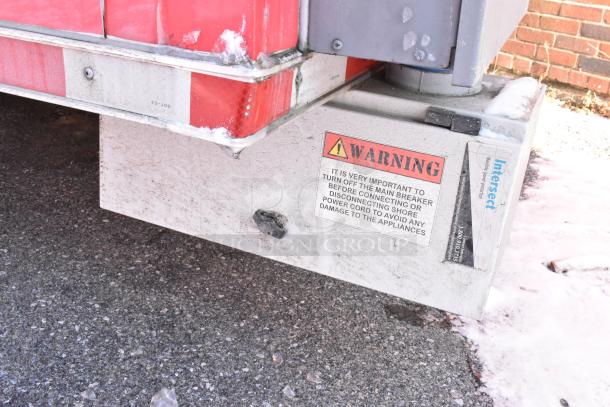 Red and white trailer detail with a warning label about turning off the main breaker before connecting power.