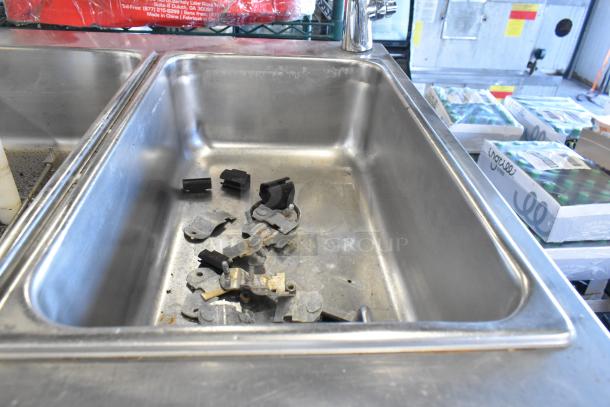 Stainless steel commercial sink with various metal fittings and rubber pieces inside.