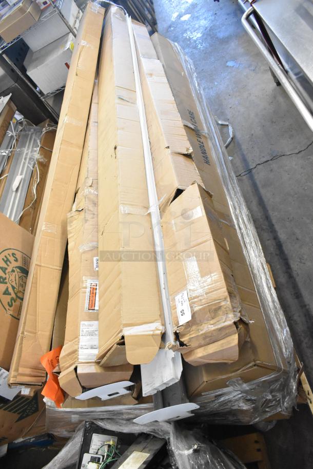 A stack of 14 brand new scratch and dent light fixtures and fluorescent tube light frames in their original packaging.