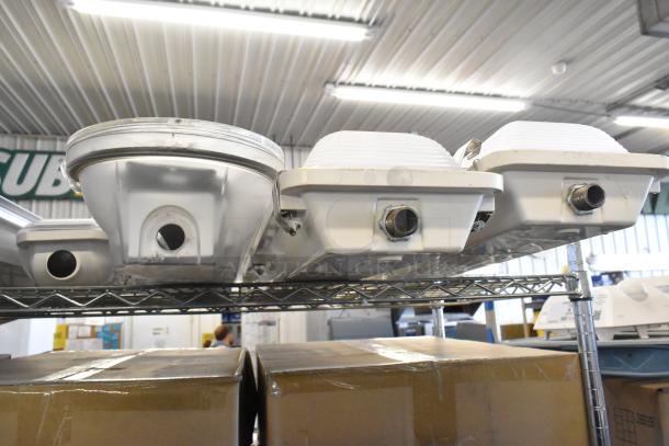 7 assorted light fixtures including Lithonia Lighting GTL 4 40L GZ10 LP840 displayed on shelf, mild wear visible.