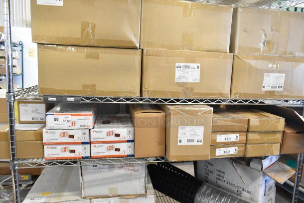 Sixteen unopened boxes containing Dual Lite LED emergency light back boxes, double remote heads, and exit signs on metal shelves. Tags show "LED Quantum" branding.
