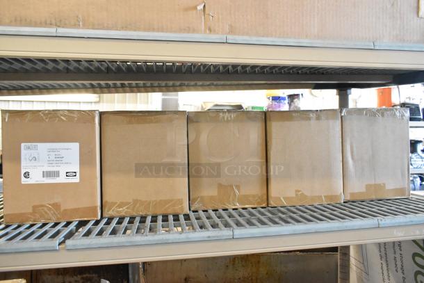 Seven new center pull towel dispensers in cardboard boxes on a shelf, labeled "Commercial LED Emergency Light" by DUAL-LITE.