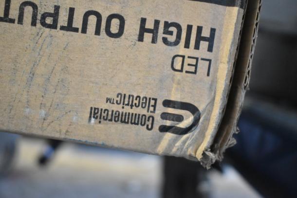 Box labeled "High Output LED" from Commercial Electric, containing various light fixtures. Box shows signs of wear.