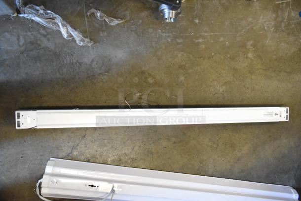 7 various light fixtures on concrete floor, including long fluorescent fixtures. Assorted conditions, ready for installation.