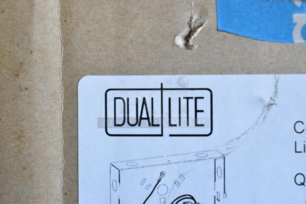 Dual Lite logo on cardboard box. Visible product diagram hints at LED emergency light components. Box shows minor scuffs.