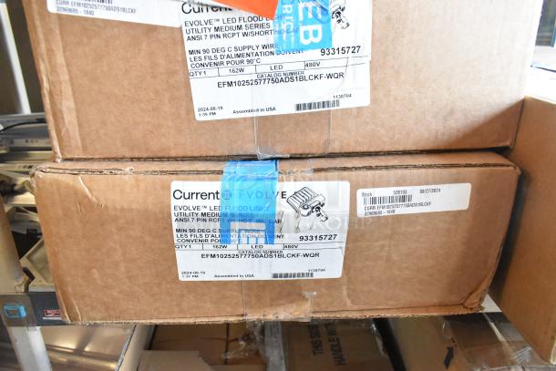 Boxes of Current Evolve LED Flood Lights, model EFM1025257750ADS1BLCKF-WQR, 162W, 480V, new condition. Tags show specifications.