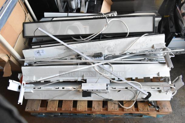 Eight white rectangular light fixtures on a pallet, various wires and components visible, used condition. Label states "QTY: 8."