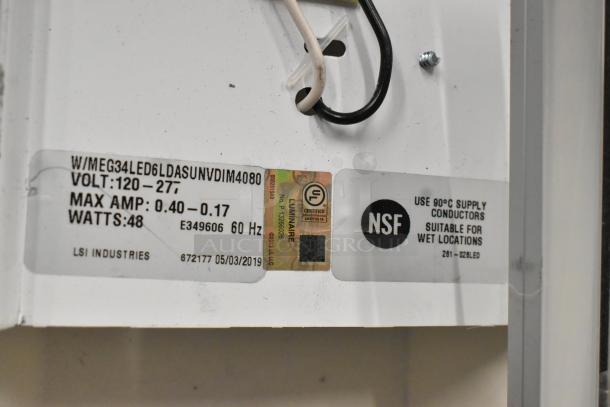 Close-up of light fixture label showing voltage range 120-277V, max amp 0.40-0.17, 48 watts, LSI Industries, NSF certified.
