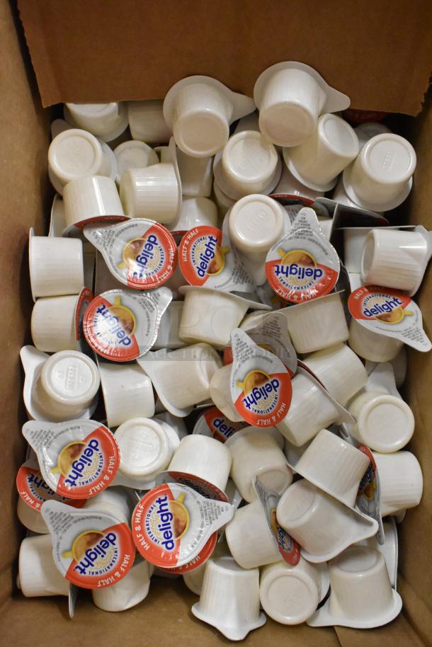 A cardboard box filled with individually sealed International Delight half & half coffee creamer cups.