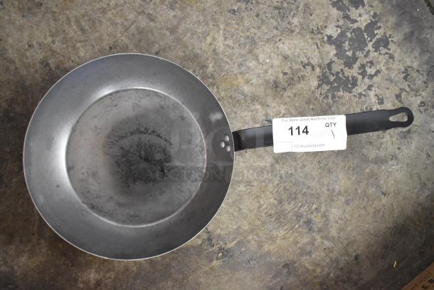 Metal skillet with a worn surface and black handle, marked "114" on the handle tag.