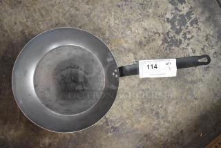 Metal skillet with a worn surface and black handle, marked "114" on the handle tag.