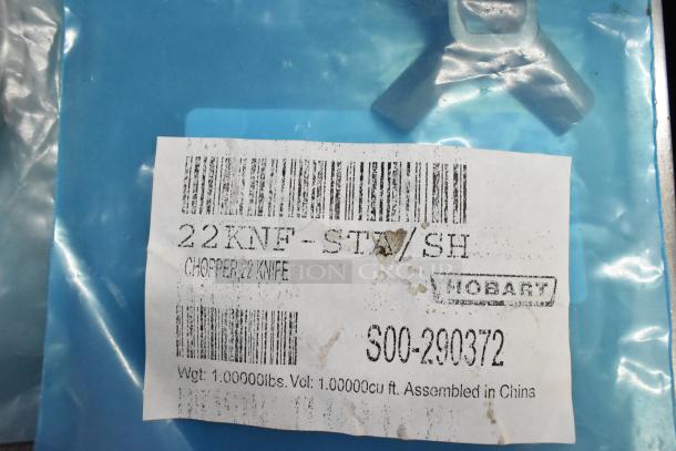 7 brand new Hobart grinder plates for meat chopper, scratch and dent condition. Label reads: "22 KNF-STX/SH" and "Chopper Knife".