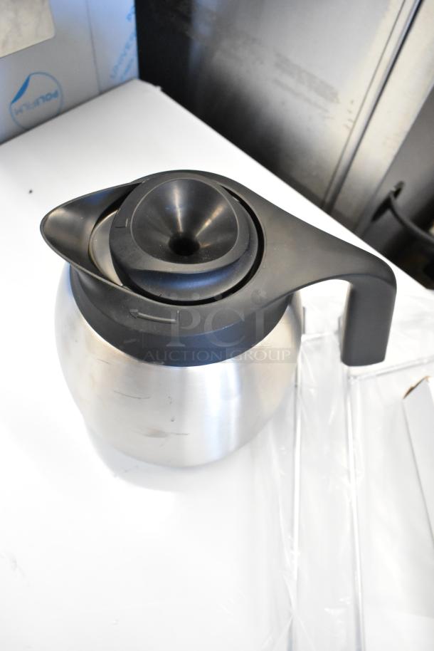 Stainless steel coffee pot with black handle and lid, part of a 4-piece auction set, new with minor scratches.