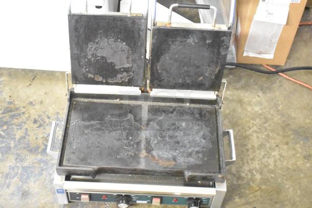 Waring WFG300 stainless steel double panini press, 240V, used condition, visible wear on grilling surfaces, dual controls.