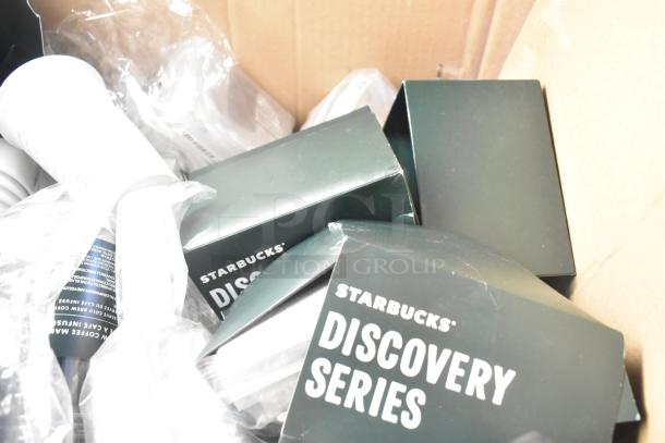 Lot of Starbucks Discovery Series items including boxed products, plastic cups, straws, and lids in a cardboard box.