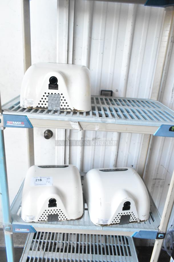 Three Xlerator XL-W white metal hand dryers, wall-mounted, 110/120 volts, 1 phase, showing minor wear. Auction tag marked "216 QTY x3" visible.
