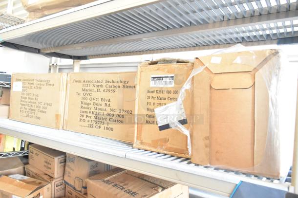 Six boxes on a metal shelf, including Betco Emulsinator stripper and K2811 000 000. Boxes have shipping labels from Associated Technology to QVC.