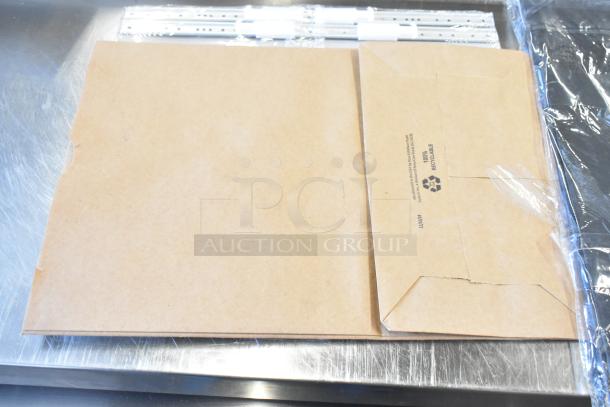 Lot of brown paper bags and Acco binders, new condition, visible 100% recyclable label on bag, stacked on metal surface.