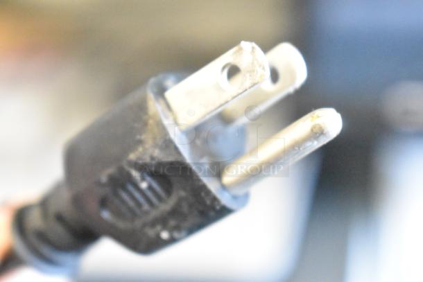 Close-up of a power plug, likely part of the Brother MFC-L6810DW Countertop Printer, showing standard three-prong design.