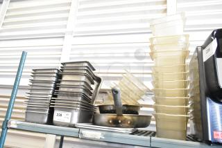 Lot of stainless steel and poly drop-in bins stacked on a shelf. Includes multiple sizes, good condition, with visible auction tags.