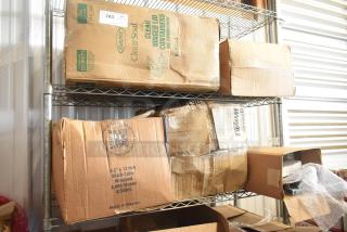 Two-tier shelf with various items, including boxes labeled "Dart ClearSeal" and "2,000 Straws," cardboard packaging, visible wear.