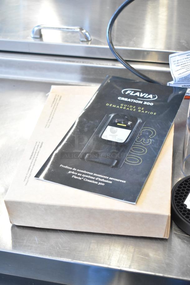 Flavia Creation 300 Quick Start Guide on cardboard box, cord visible, on stainless steel surface.