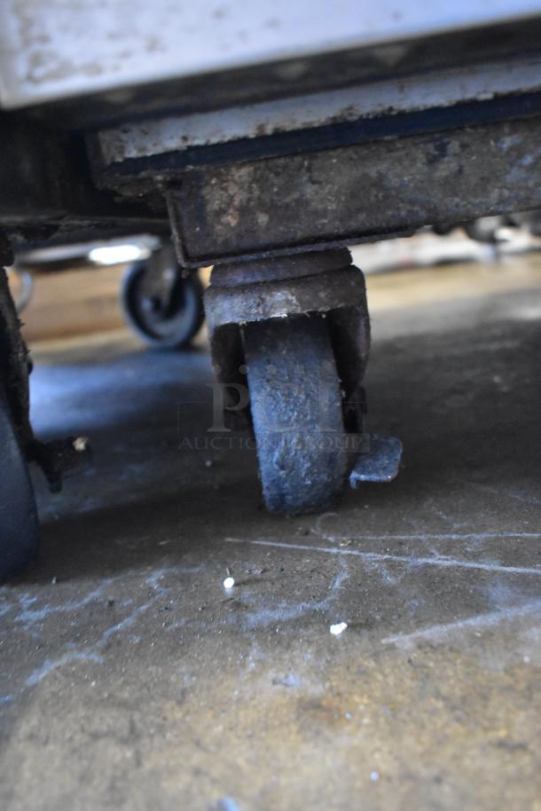 Close-up of a commercial caster on a True TM-24 stainless steel cooler. Caster shows signs of wear, supporting mobility.