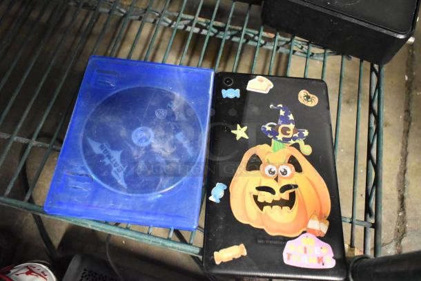 A decorated Halloween-themed tablet cover and a blue Batman DVD case on a wire shelf.