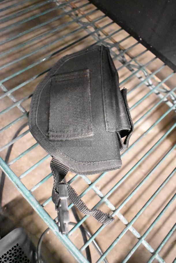 A black nylon holster with a clip, placed on a wire shelf. Simple design, condition not specified.