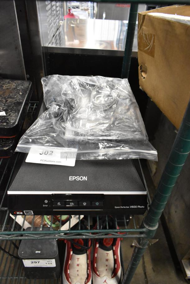 Epson J252A Photo Scanner, model V600, on shelf, with power cable in plastic bag. Appears in used condition.