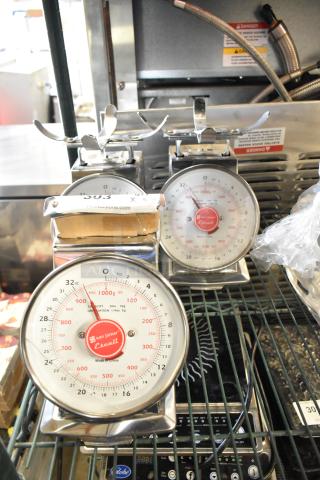 Three stainless steel countertop scales, San Jamar Escali brand, each in good condition with red dial and measurement markings.