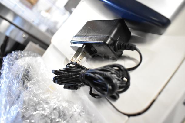 Power adapter with coiled cable, possibly for the AccuBanker D450 Counterfeit Bill Detector, on a white surface.