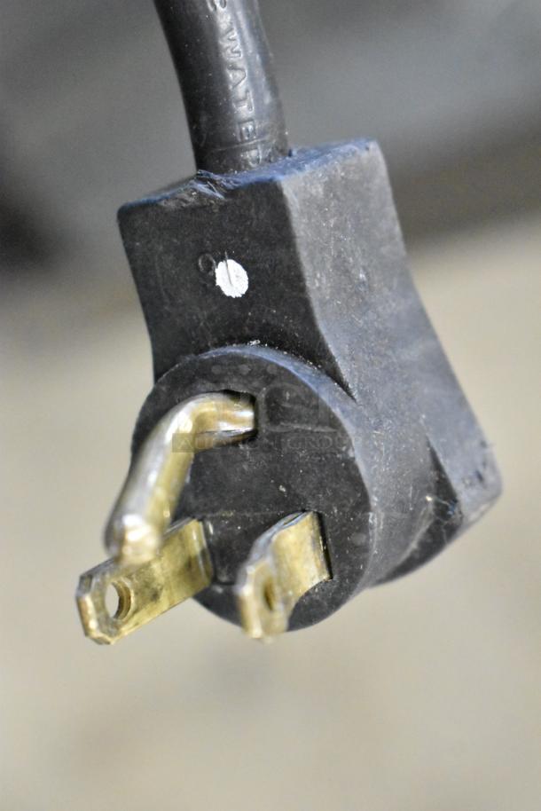 Close-up of a power plug from a Beverage Air SPE48-18M-HMP prep table, showing brass prongs and a black plastic body.