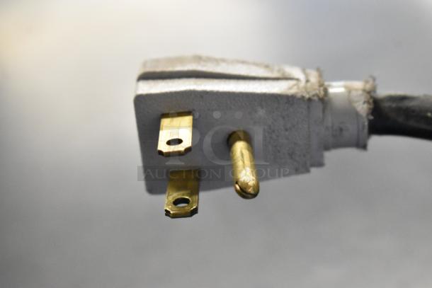 Close-up of a white and gold power plug for a True GDM-41SL-48-HC-LD cooler, showing three-prong configuration.