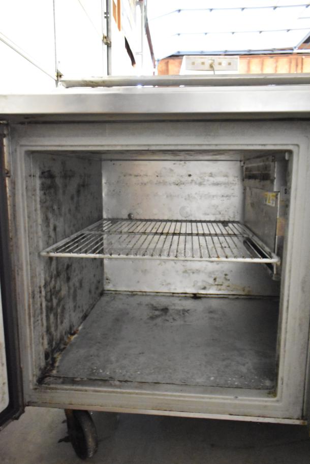 Randell stainless steel commercial pizza prep table, open interior view, showing shelving inside. Mounted on commercial casters.