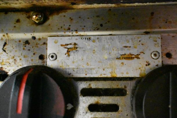 MagiKitch'n stainless steel commercial charbroiler grill with gas control knobs. Visible wear and rust marks around panel.