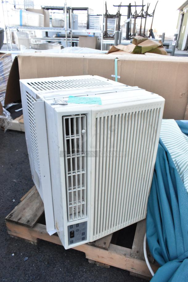 White air conditioner unit on a wooden pallet, showing vents and control panel. Includes multiple items in background.