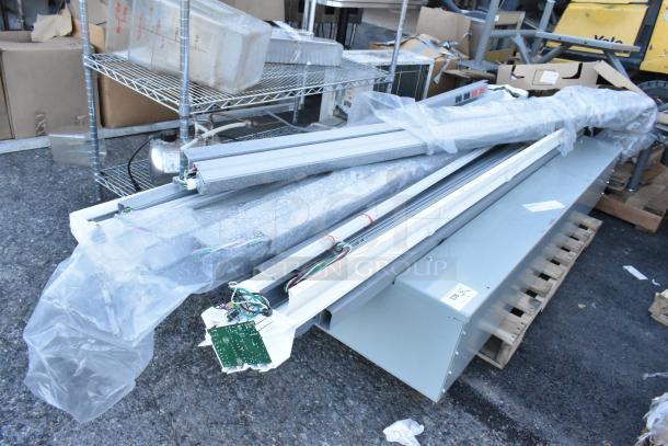 Assorted light fixtures in packaging with a gray metal unit, displayed on a pallet. Items appear in new condition.