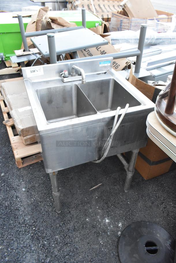Stainless steel 2 bay sink with faucet and handles. Features dual basins, industrial-grade design, and visible plumbing hoses.