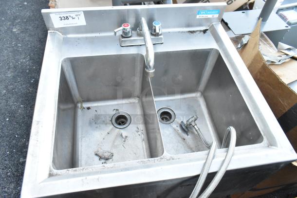 Stainless steel 2-bay sink with central faucet and handles, marked BK Resources. Slight wear, includes attached hoses.