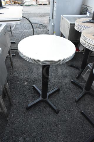 Six round tables with black metal bases, shown on outdoor pavement. White tops, stackable. Good condition.