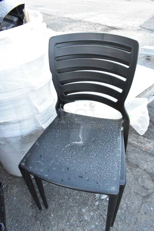 Black poly chair with textured seat and slatted backrest, next to white poly trash can in a lot of various items.