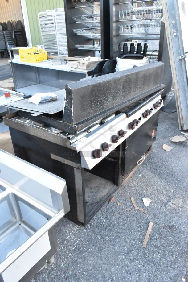 Wolf metal commercial gas range with 6 burners, flat top griddle, oven, backsplash, and overshelf. Used condition.