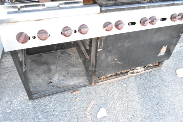Wolf commercial gas range with 6 burners, flat top griddle, oven, backsplash, overshelf. Shows signs of wear and rust.